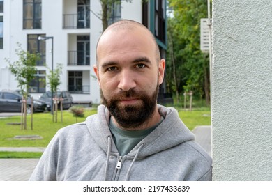 Portrait Of A Serious Man 30-35 Years Old With A Beard On The Background Of Beautiful High - Rise Building And Green Trees.