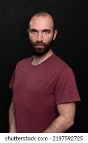 Portrait Of A Serious Man 30-35 Years Old In A T-shirt, Bald And With A Beard On A Black Background.