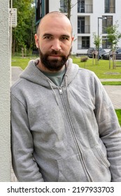 Portrait Of A Serious Man 30-35 Years Old With A Beard, Leaning His Shoulder Against The Wall, Against The Background Of Beautiful Multi-storey Buildings.