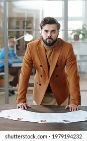 Portrait of serious man with beard wearing turtleneck and jacket leaning on table with CVS, he being responsible for recruiting specialists