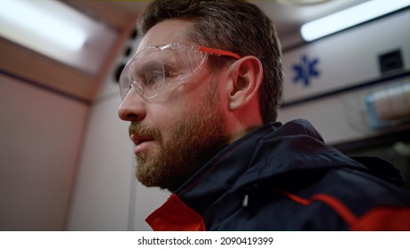 Portrait Of Serious Medical Assistant Having Conversation With Colleague. Emergency Care Doctor Discussing Job In Ambulance Vehicle. Closeup Male Paramedic Working At Night Shift. Rescue Concept