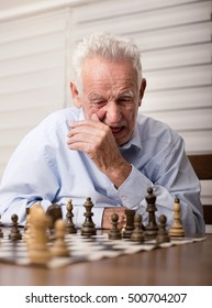 Portrait Of Serious Old Man Playing Chess In Room