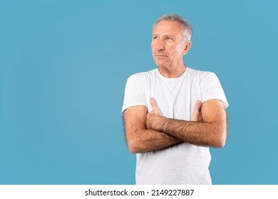 Portrait Of Serious Pensive Mature Man Posing With Folded Arms, Looking Away At Free Copy Space Mockup, Standing Isolated On Blue Studio Background. Confident Male Adult Holding Hands Crossed