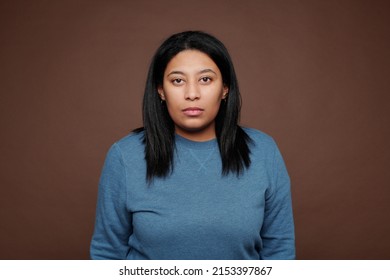 Portrait Of Serious Portly Black Woman In Blue Sweater Standing Against Isolated Brown Background