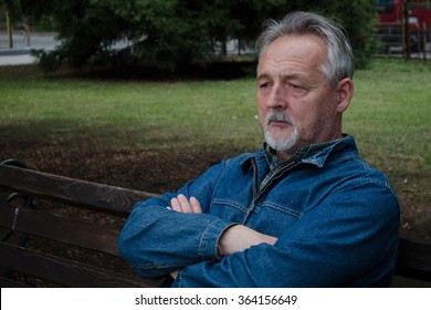 Portrait of a serious senior man sitting in the park, thinking and looking far away. Outdoors.