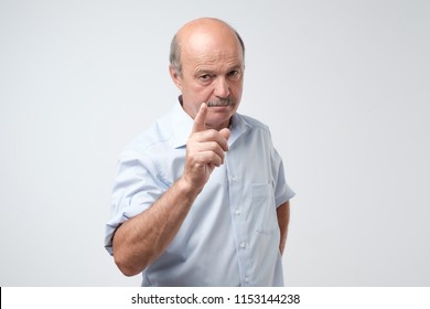Portrait of serious senior man with warning finger and blue shirt shirt against light gray background. You better listen to my advice concept