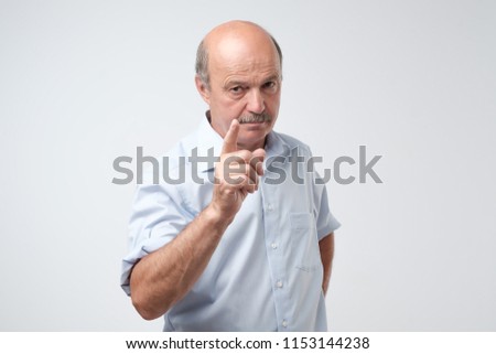 Portrait of serious senior man with warning finger and blue shirt shirt against light gray background. You better listen to my advice concept