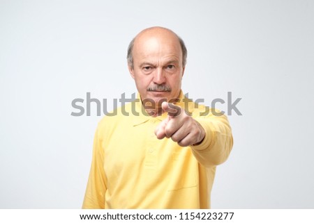 Portrait of serious senior man with warning finger and yellow t-shirt shirt against light gray background. You better listen to my advice concept