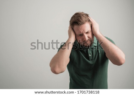 Portrait of serious stylish attractive man with thick beard, dressed in casual green t shirt gesturing head ache isolated on gray background with copy space advertising area