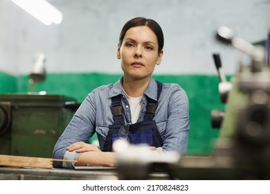 Portrait of serious tenacious lady engineer with brown hair leaning on table at factory workshop - Shutterstock ID 2170824823