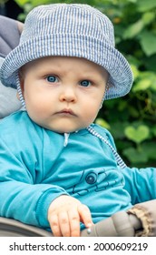 Portrait Of Serious Unsmiling Baby Wearing Sunhat And Sitting In The Baby Buggy. 