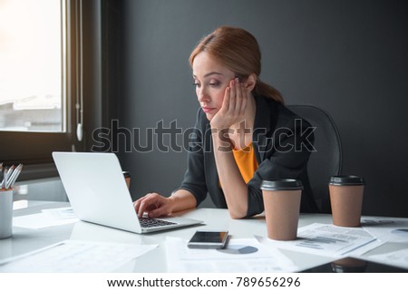 Portrait of serious weary businesswoman typing in laptop while sitting at table in apartment. Occupation and weariness concept