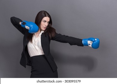 Portrait Of Serious Woman In Gloves. Young Businesswoman In Blue Boxing Gloves As A Metaphor For Office Politics On Grey Background.