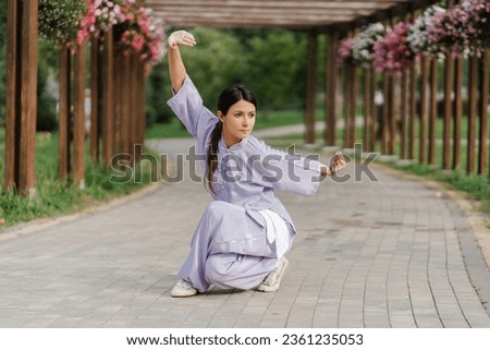 Portrait of serious woman wearing  kimono training, practicing wushu in park. Healthy lifestyle, kungfu, martial arts concept 