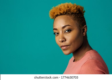 Portrait of a serious young african female with cool short hair looking at camera, against studio background