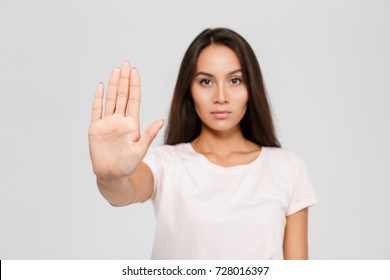 Portrait of a serious young asian woman standing with outstretched hand showing stop gesture isolated over white background, focus on hand - Powered by Shutterstock