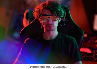 Portrait Of Serious Young Caucasian Man In Neon Rave Glasses Sitting In Computer Chair