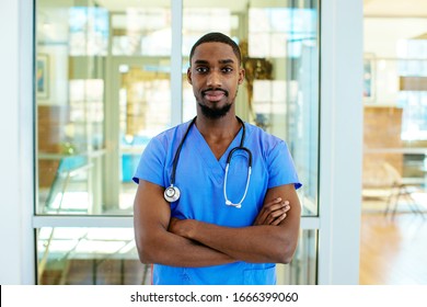 Portrait of a serious young male doctor or nurse wearing blue scrubs uniform and stethoscope, with arms crossed in hospital