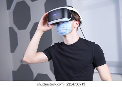 Portrait Of Serious Young Man, Guy Using, Wearing A Modern Device Virtual Reality Headset Mask 3D, AR, VR Glasses, Playing The Game In Medical Mask On Face. Technology Metaverse, Coronavirus, Covid-19