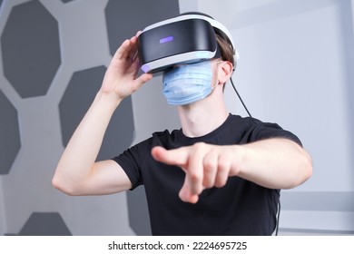 Portrait Of Serious Young Man, Guy Using, Wearing A Modern Device Virtual Reality Headset Mask 3D, AR, VR Glasses, Playing The Game In Medical Mask On Face. Technology Metaverse, Coronavirus, Covid-19