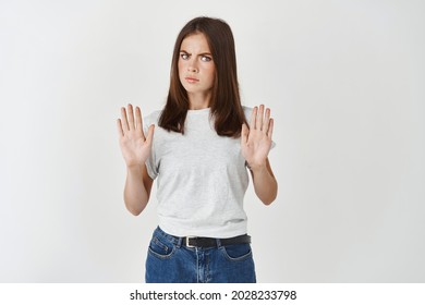 Portrait Of A Serious Young Woman Standing With Outstretched Hand Showing Stop Gesture Isolated Over White Background, Strongly Refuse And Saying No