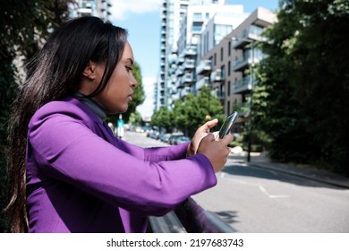 Portrait Of Serious Young  Woman Using Her Mobile Phone Leaning On A Banister In A Street Of London.