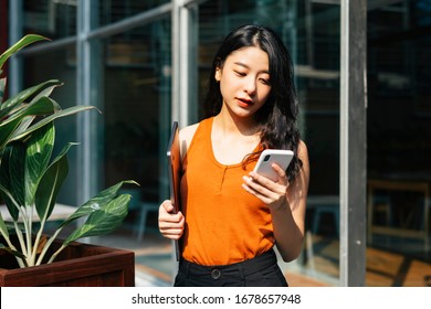 Portrait Of Sexy Asian Beautiful Woman Wearing Orange Shirt Holding Laptop, Talking On The Phone At Cafe Garden In The City.