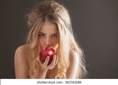 Portrait of a sexy beautiful nude pin-up girl from 60s or 70s, eating and biting a fresh red apple with temptation on dark background.