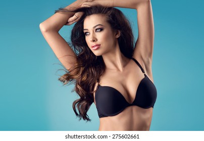 portrait of sexy brunette woman with a perfect body and large breasts posing in black lingerie on a blue studio background