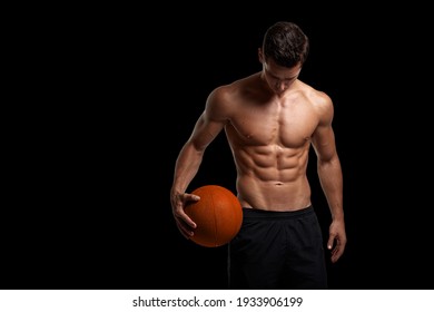 Portrait of a sexy handsome brunette young man with muscular body holding a bascket ball, posing at studio. Black background. Men's health.