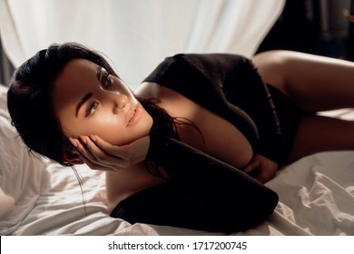 Portrait Of A Sexy And Luscious Woman Laying In A Black Leotard Costume Among Bed Sheets And Holding Her Dark Brown Hair With Hand