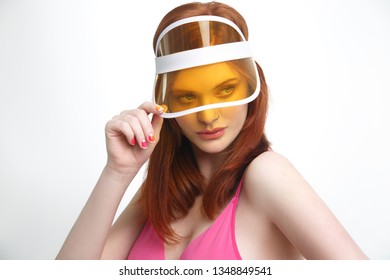 Portrait of a sexy red-haired girl in a transparent yellow sun visor isolated on a white background.