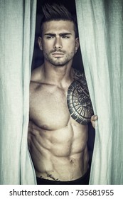Portrait of sexy shirtless muscular man next to window curtains during the day, wearing only jeans