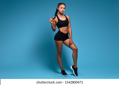 Portrait Of Sexy Slim Woman In Black Fashion Sportswear Posing In Studio. Full Length Photo. Isolated Blue Background, Studio Shot. Lifesstyle, Free Time, Spare Time