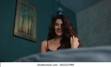 Portrait of sexy woman biting lip in bed. Closeup long hair girl having fun in hotel bedroom in slow motion. Sensual model flirting with camera on bed in modern interior.