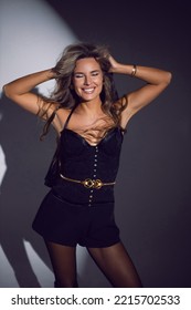 Portrait Of A Sexy Woman In A Black Corset, Shorts And Boots Stands In The Studio On A White Cyclorama With A Light Spot