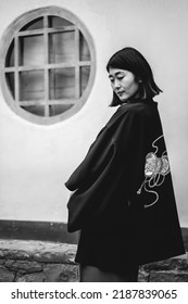 Portrait of sexy and young japanese girl with beautiful old traditional red kimono and black yukata in front of a old white wall in a japanese garden (in black and white)