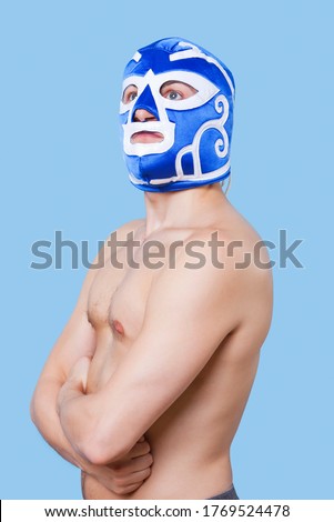 Portrait of shirtless man in wrestling mask gesturing over gray background