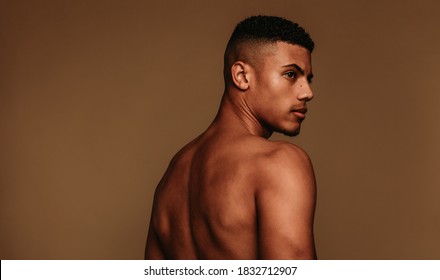 Portrait of shirtless muscular man looking away. Side view of african american man standing on brown background.
