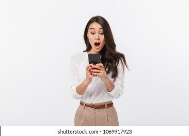 Portrait of a shocked asian businesswoman using mobile phone isolated over white background