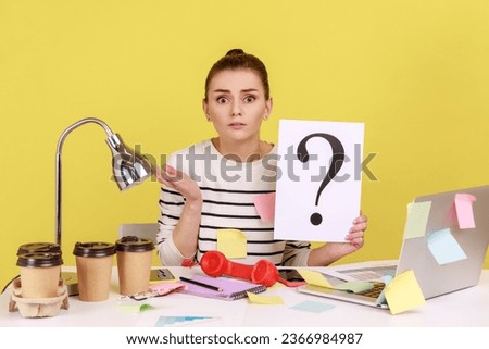 Portrait of shocked astonished woman looking at camera, holding paper with question mark, thinks about tasks, covered with sticky notes. Indoor studio studio shot isolated on yellow background.