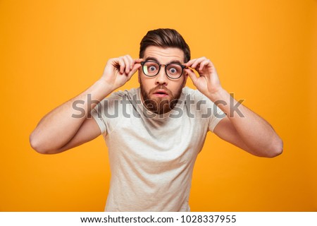 Portrait of a shocked bearded man in eyeglasses looking at camera isolated over yellow background