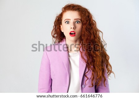 Portrait of shocked beautiful business woman with red - brown hair and makeup in pink suit. looking at camera, studio shot on gray background.