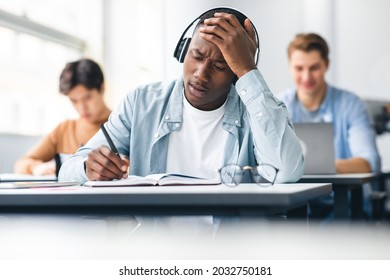 Portrait Of Shocked Black Student In Headphones Sitting At Table In Classroom, Touching Forehead In Panic, Writing Entrance Exam Looking At Hard Questions Or Test Result, Thinking About Right Answer