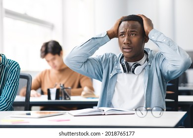 Portrait of shocked black student sitting at desk in classroom, grabbing his head. Sad African American youth unprepared for test or exam, thinking about deadline or hard new theme