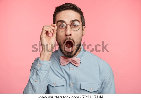 Portrait of shocked stupefied young bearded male model stares at camera as forgets some importnat information, keeps mouth widely opened, dressed in elegant clothes, isolated over pink background