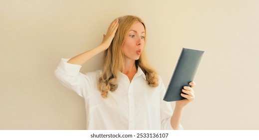 Portrait of shocked and surprised caucasian young woman employee looking at digital tablet computer or folder with documents, emotional overworked office manager - Powered by Shutterstock