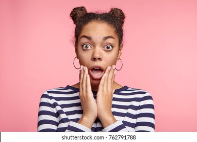 Portrait of shocked woman with dark skin and two hair knots, being surprised or astonished to see large discounrs at shop, isolated over pink background. Great disbeief and surprisment concept.