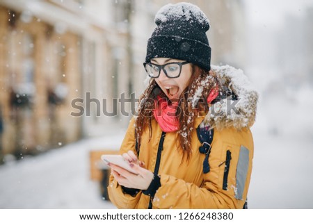 Portrait of shocked woman with red hair looking camera mobile phone in hand she has some good news message with stunned emotion on face finger up saying attention city background.