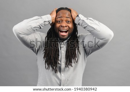 Portrait of shocked young African American man with dreadlocks wearing shirt looking at the camera in surprise, stunned with some incredible story, holding hands on head, human expressions emotions